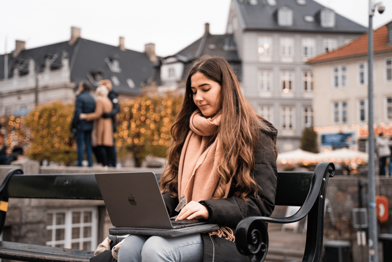 Kvinde sidder på en bænk i byen og arbejder på sin MacBook.