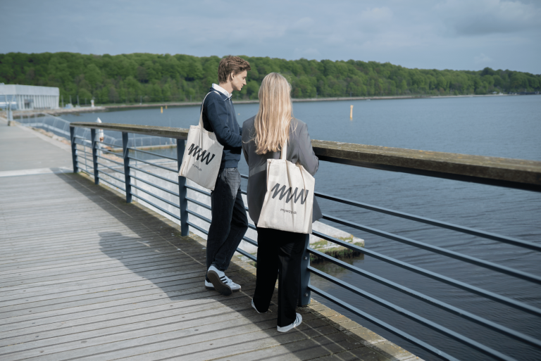 To unge står ved havnefronten med myway-tasker over skulderen.