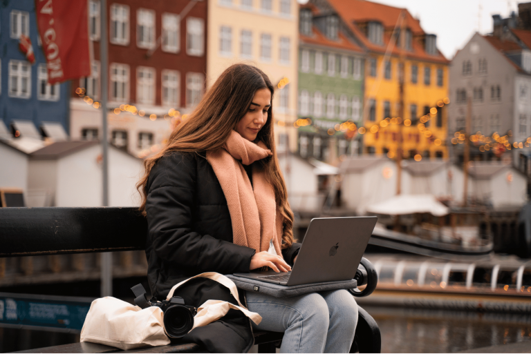 Kvinde arbejder på sin MacBook udendørs ved kanalen i København.