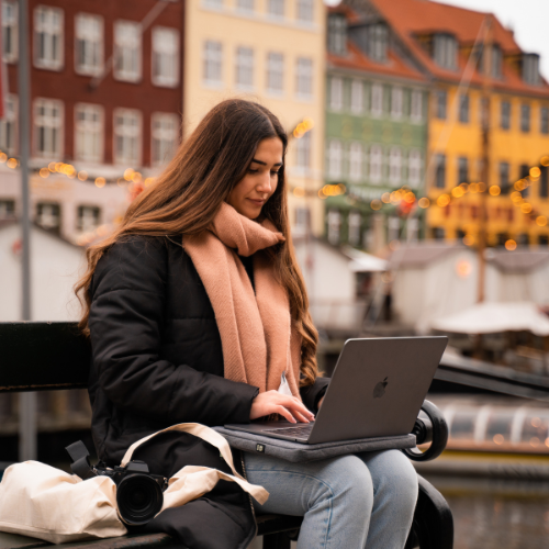 Ung kvinde arbejder på en MacBook udendørs ved havnen