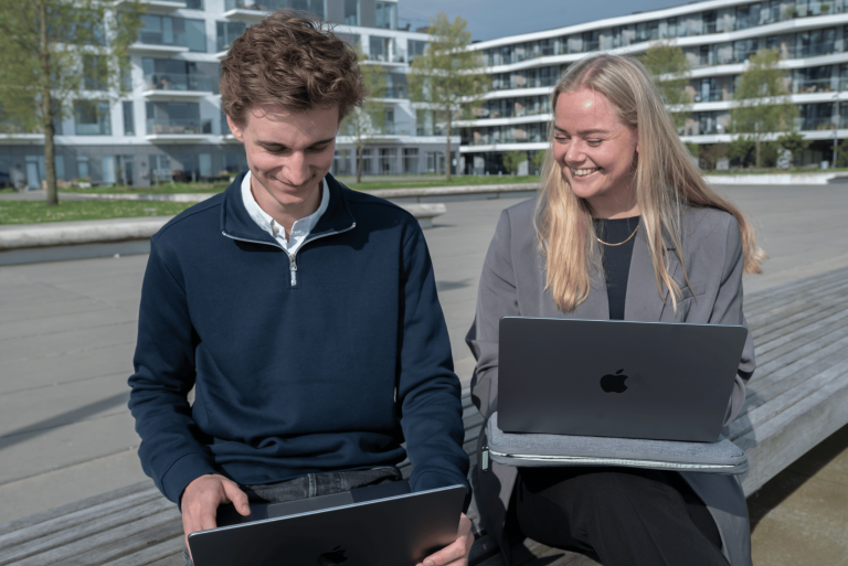 To unge sidder udendørs og arbejder på deres MacBooks.