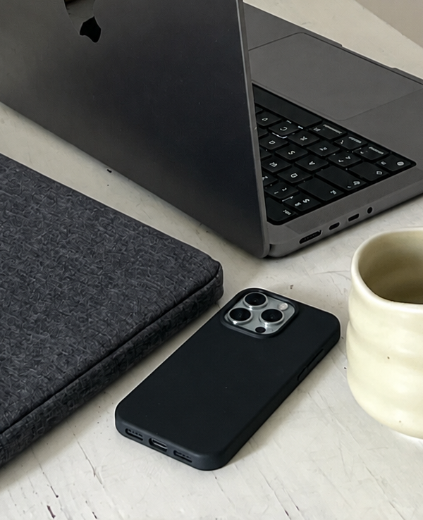 iphone 15 pro ligger på bord med computer og kop